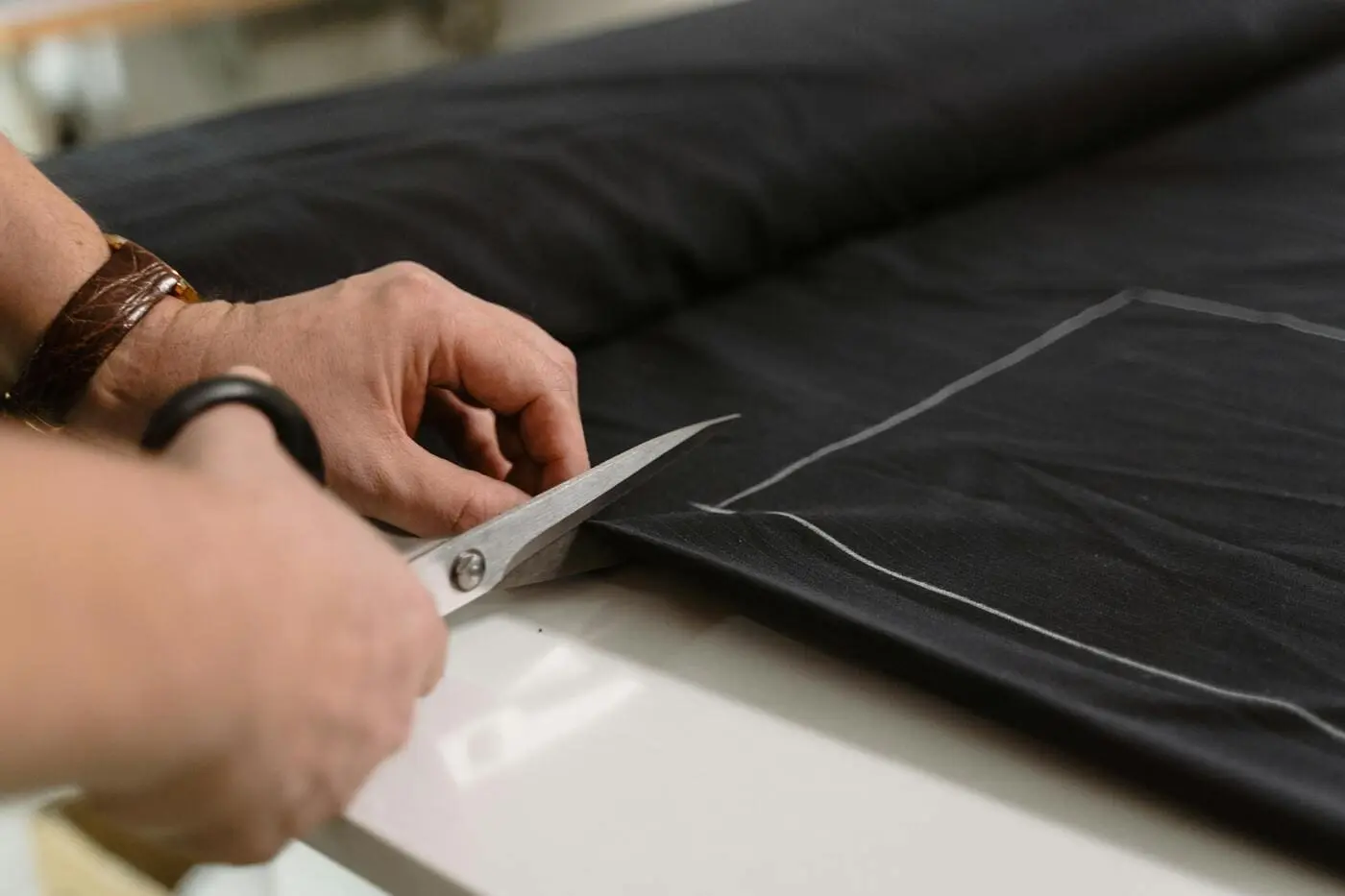 Mains découpant un tissu avec des ciseaux en suivant des lignes de patron.