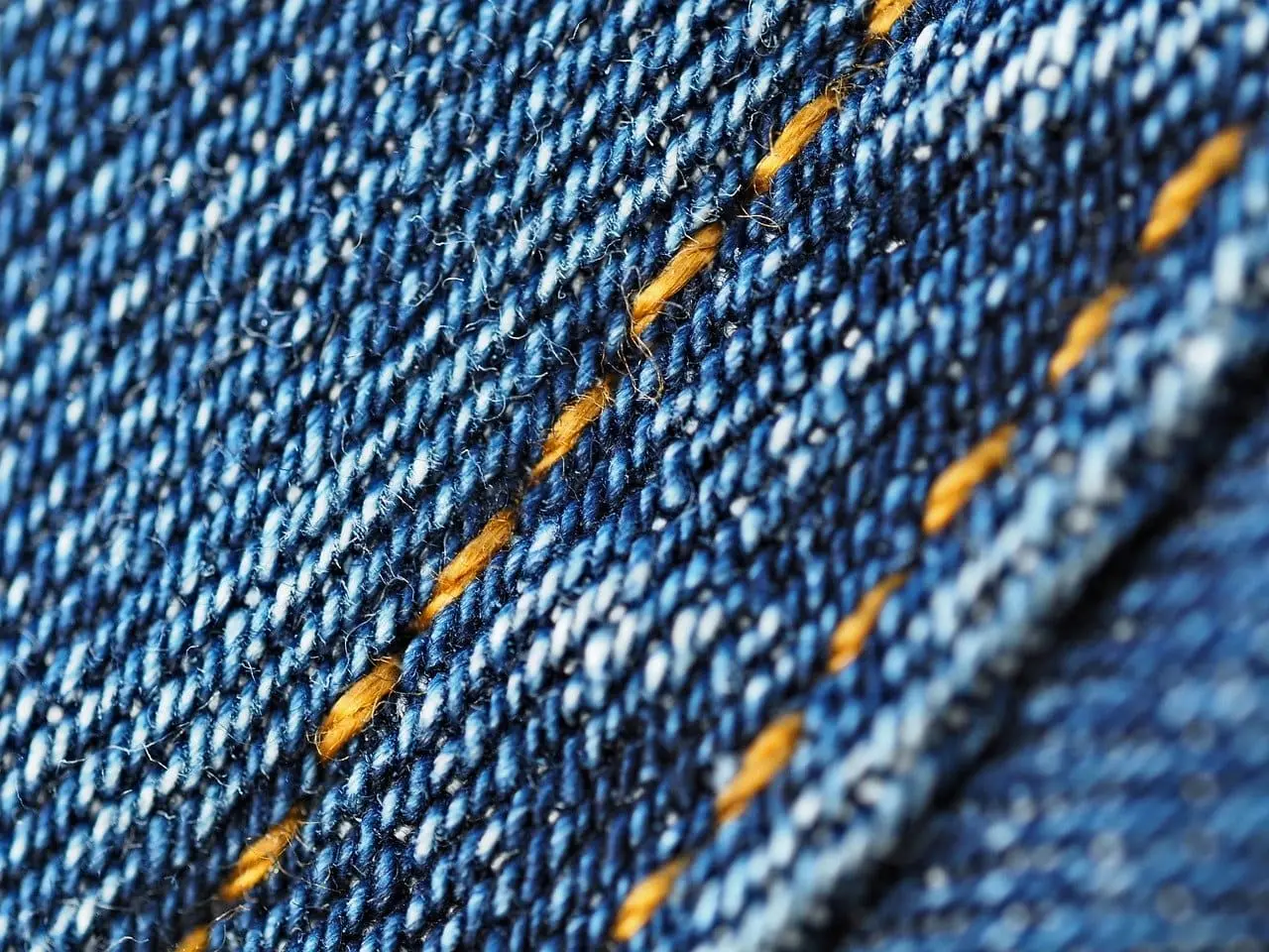 Gros plan d’un tissu en jean bleu avec couture jaune.