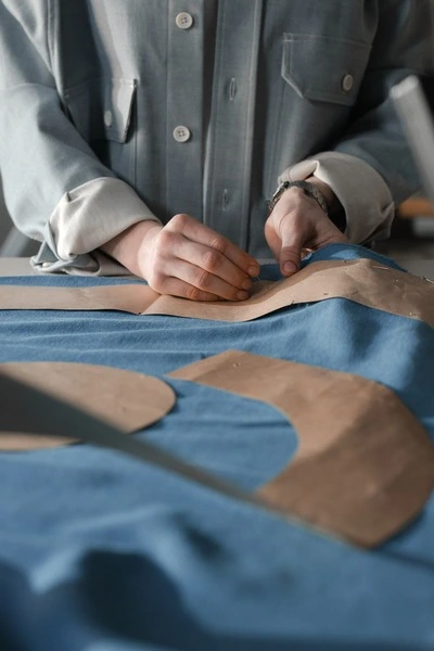 Une personne positionne et épingle un patron en papier sur un tissu en denim bleu avant la découpe, illustrant une étape de préparation en confection textile.